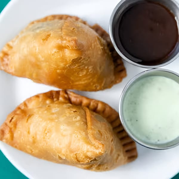 Two golden-brown samosas with dark and light green dipping sauces on a white plate.