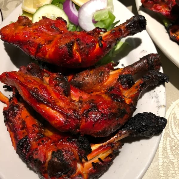Three pieces of Darbar Boston's Tandoori Chicken, garnished with lemon, cucumber, and red onion.