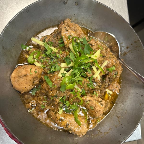 Pakistani chicken karahi, garnished with green chilies, ginger, and cilantro, in a metal wok.