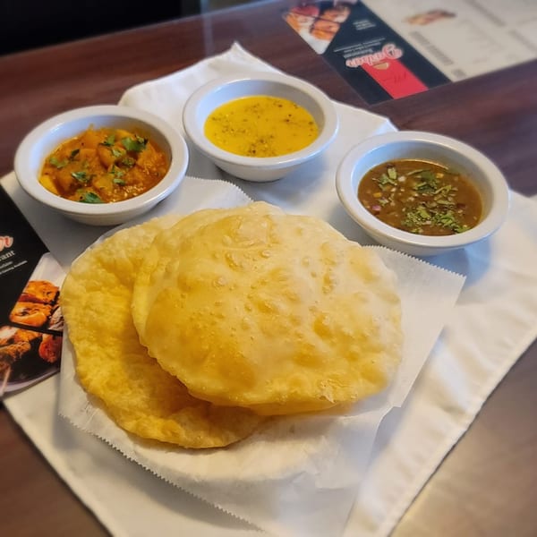 Pakistani puri bread with three small bowls of curry and sauces on a white napkin.