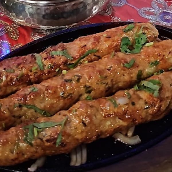 Three sizzling seekh kebabs garnished with cilantro on a black platter at Darbar Boston.