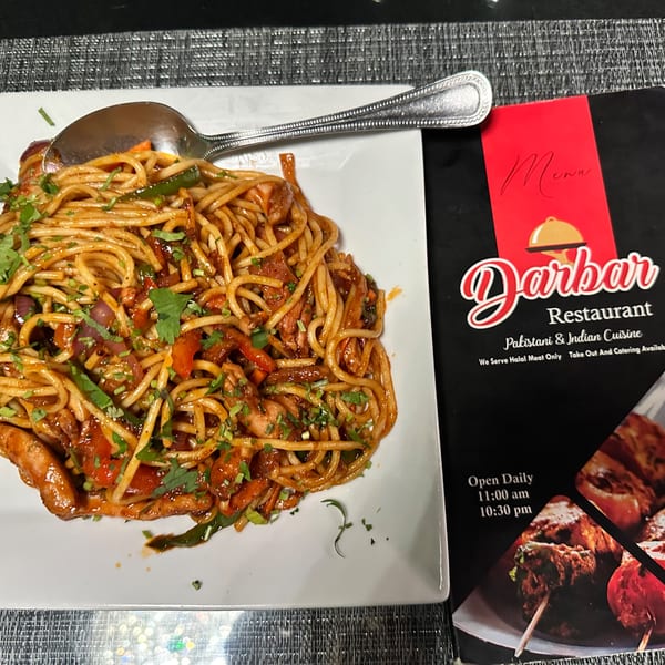 A plate of Pakistani noodles with vegetables and chicken, next to a Darbar Restaurant menu.